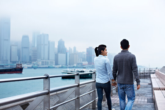 Couple, walk and holding hands on promenade for vacation, date and back for sightseeing or bonding. Man, woman and tourist with trip, holiday and travel for honeymoon or romance at waterfront
