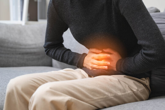Close-up hands of young woman putting on her belly and feeling pain from cycle period on the sofa.