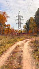 Obraz premium Dirt path winds through autumn forest. Electric tower stands tall against blue sky.