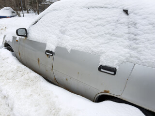 Obraz premium Snow blankets a rusted silver car. Snow covers the car's roof and sides.