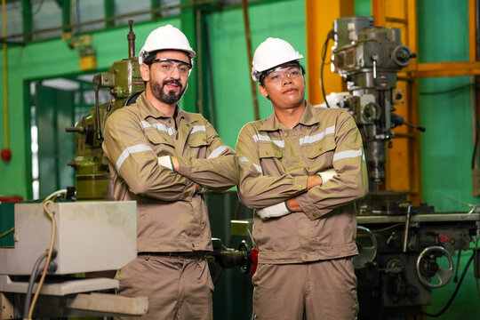 Engineer worker factory hard hat uniform machinery industry workshop safety team, male and female engineer stand with crossed arm near industrial machine in factory workshop