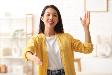 Beautiful young Asian woman waving and extending hand for handshake at home © Pixel-Shot