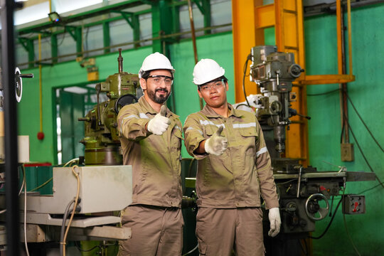 Engineer factory worker hard hat machine Engineer factory worker hard hat machine inside industrial workshop, two male technician wearing safety gear and glove, positive gesture near metal