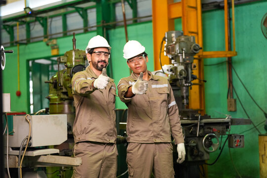Engineer worker hard hat factory machinery uniform glove thumbs up industrial workshop two male engineers safety gear show confident thumbs up inside manufacturing workshop with metal machine
