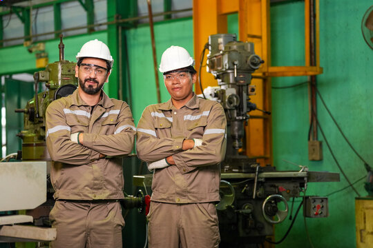 Engineer worker factory helmet uniform machine industry teamwork Two industrial technicians with arms crossed inside workshop near heavy equipment