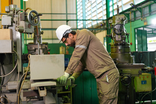 Engineer factory machine worker hard hat glove industrial workshop maintenance manufacturing scene with focused technician operating metal equipment