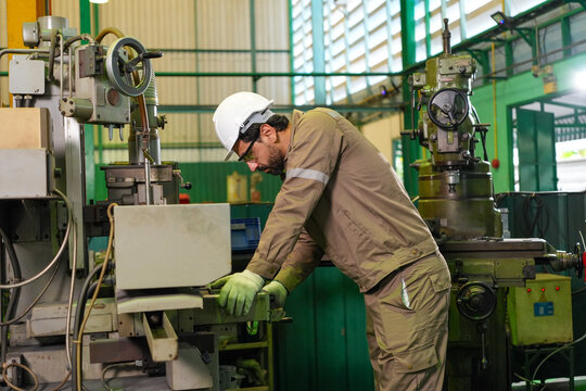 Engineer worker factory machine helmet glove workshop industrial technician operating metal equipment inside production plant with focused posture