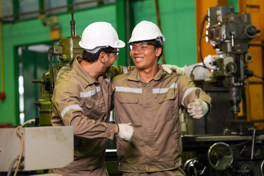 Engineer worker hard hat factory machine uniform Two cheerful industrial workers talk beside heavy equipment in manufacturing workshop