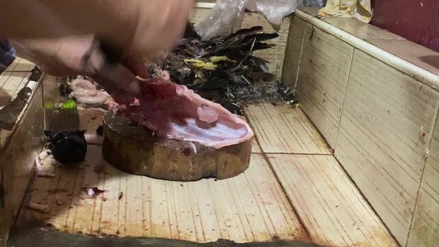 Dressed chicken meat is being chopped into pieces in a messy and disorganized Asian wet market.