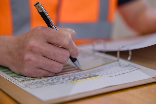 Warehouse worker reviewing and signing logistics documents representing inventory management, inspection, paperwork, supply chain operations, quality control industrial business workflow.