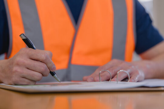 Warehouse worker reviewing and signing logistics documents representing inventory management, inspection, paperwork, supply chain operations, quality control industrial business workflow.