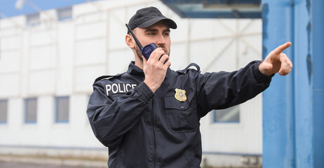 Police officer in uniform communicating on a walkie-talkie and pointing, Security and law...