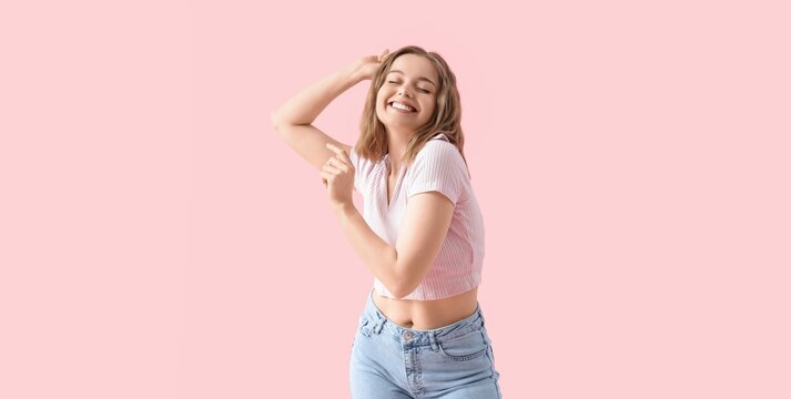 Happy young woman with closed eyes and arms raised, expressing joy and freedom on a pink background