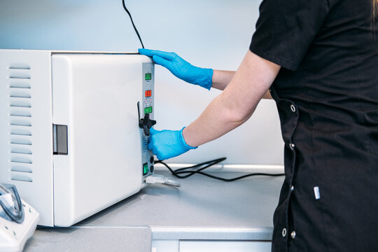 Gloved hands operate control panel of medical autoclave machine in clinic laboratory. Setting autoclave cycle, adjusting sterilization parameters, dental sterilizer control panel operation.