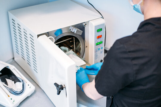 Person operates open autoclave sterilizer machine in medical office. Dental sterilization equipment, clinic technician workflow, behind the scenes dental practice.