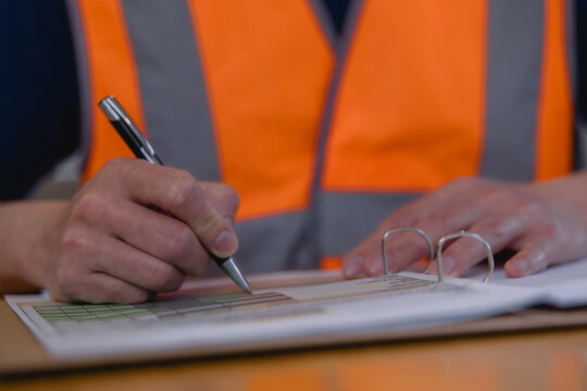 Warehouse worker reviewing and signing logistics documents representing inventory management, inspection, paperwork, supply chain operations, quality control industrial business workflow.