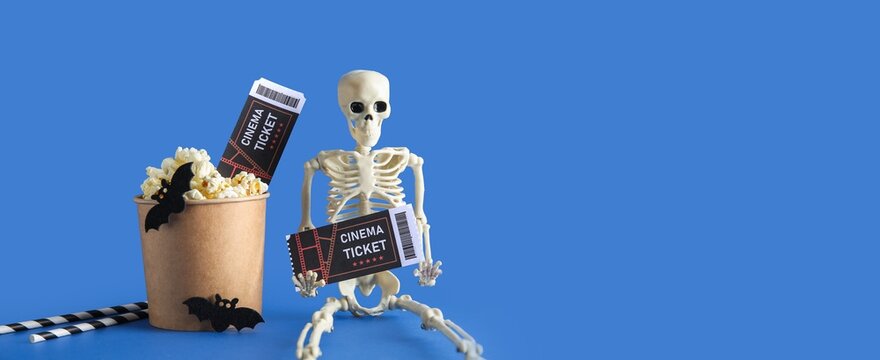 Halloween skeleton holding cinema tickets with popcorn and bat decorations for a spooky movie night on a blue background