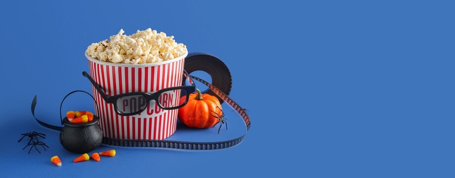 Halloween movie night with popcorn, 3d glasses, film reel, candy corn, and decorative pumpkin on blue background