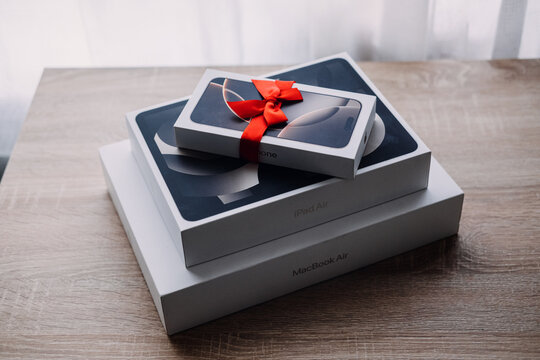 iPhone box with red ribbon bow sits on iPad Air and MacBook Air boxes on table. Apple devices with gift bow, iphone ipad macbook gift set, tech bundle holiday gift. Warsaw, Poland, 20 July 2026.