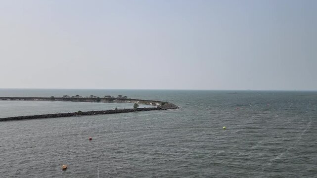 Serene coastal scene featuring a calm ocean extending to the horizon with a curved pier or breakwater structure creating a peaceful and inviting atmosphere for relaxation and outdoor activities