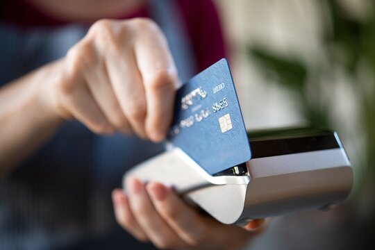 Person making payment with blue credit card at wireless point of sale retail payment terminal, contactless