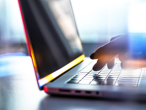 Unrecognizable man types on a laptop keyboard indoors