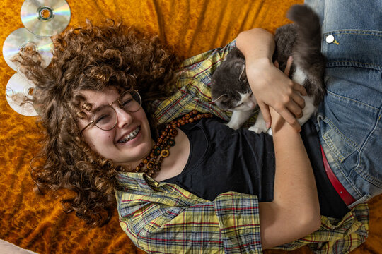 A smiling teenage girl hugs a cat while lying down with music