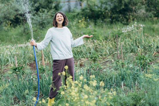 A mature woman laughs while watering plants in the summer garden