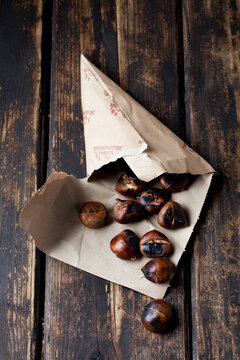 Paper bag with roasted chestnuts on dark wood