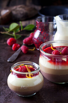 Glasses of pudding with vanilla sauce and raspberry sauce garnished with raspberries and orange zest