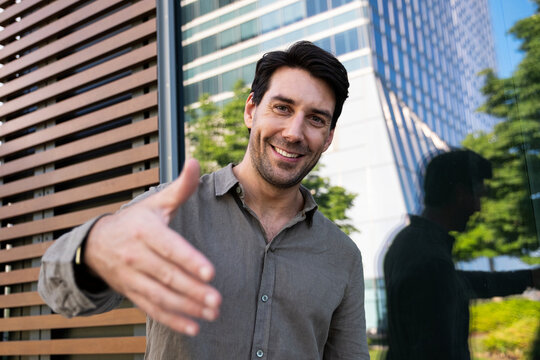 Smiling man offers a handshake outdoors in the city