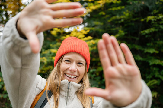 A smiling female frames the autumn forest with her hands