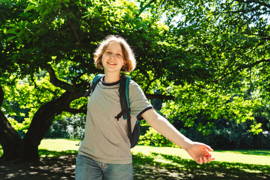 A smiling girl wears a backpack in a sunny summer park