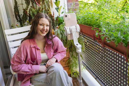 Smiling woman records a social media vlog on a tiny balcony
