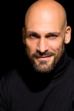 Portrait of bald man wearing black turtleneck in front of black background