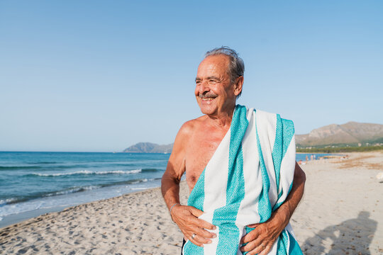 A happy senior man holds a towel on the beach