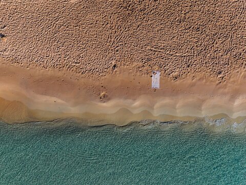 Aerial view reveals an empty sandy beach with a white towel