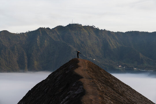 Woman walking along volcanic crater ridge at sunrise in Java Indonesia