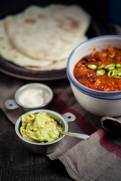 Tortillas and bowls of guacamole, sour cream, Chili con carne on wooden table