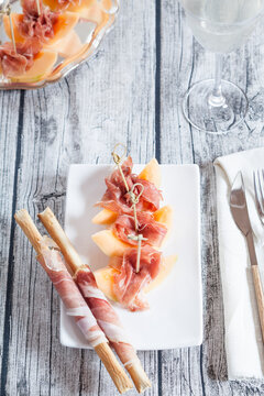 Plate of Charentais melon slices with ham and Grissini wrapped with ham