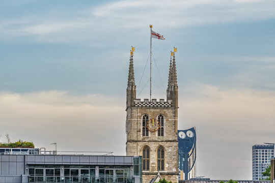 View of the historic tower of Southwark Cathedral with the St George's Cross flag flying against a blue sky in London, England, United Kingdom.