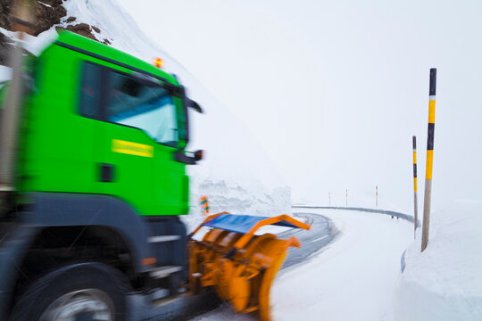 Green snowplow clears snow on a sinuous alpine road in Switzerland