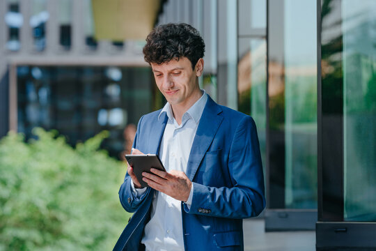 Smiling businessman uses digital tablet outdoors near building