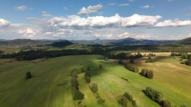 Broad green meadows and mown fields with distant hills under a wide cloudy sky