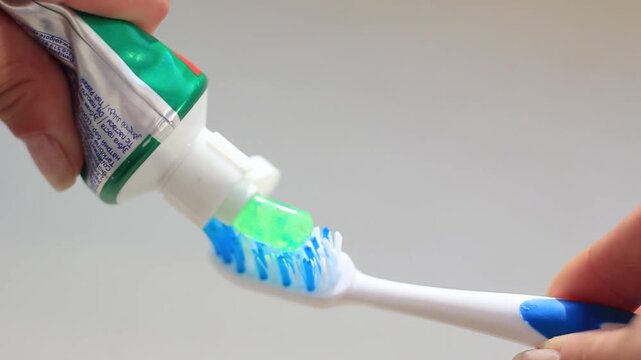 A close-up view of a toothbrush being squeezed with green and blue toothpaste.