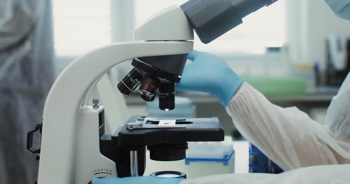 A close-up view of a laboratory microscope being operated by a researcher in a lab setting.