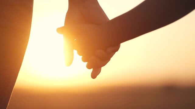 A person holding hands in the sunset. Mom, holds, daughter, hands walk, park. Mom and daughter walking in the park. The photo is of lifestyle a mother and child holding hands at sunset.