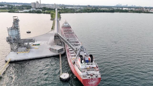 An aerial drone shot flies forward and pans down close-up over the superstructure of the CSL Tadoussac cargo ship docked at the industrial port pier in Mississauga