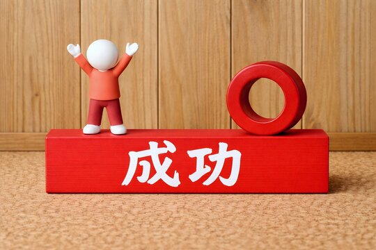 赤い積み木の上で万歳をして成功を喜ぶ粘土人形と合格や正解を意味する赤い丸の記号