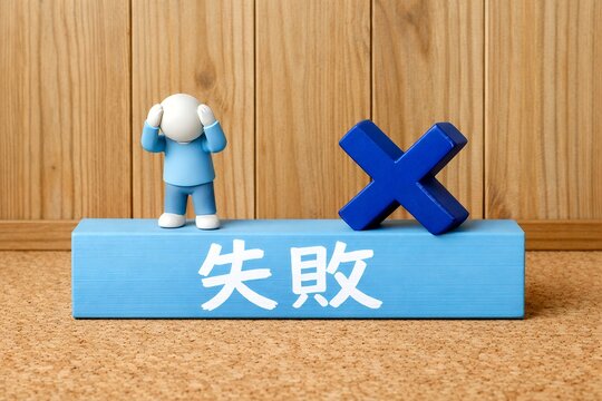 失敗という文字が書かれた青い積み木の上で頭を抱えて悩み落ち込む青い服の人形とバツ印